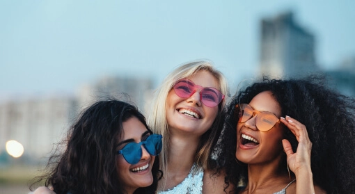 Trzy roześmiane kobiety w kolorowych okularach przeciwsłonecznych