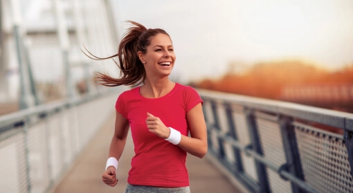 Uśmiechnięta dziewczyna w czerwonej koszulce biegnie przez most