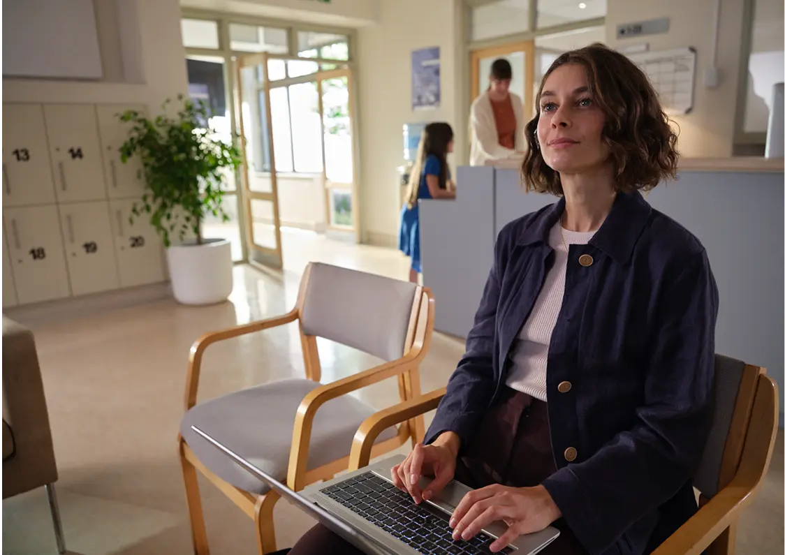 Kobieta siedząca z laptopem na kolanach w poczekalni w przychodni